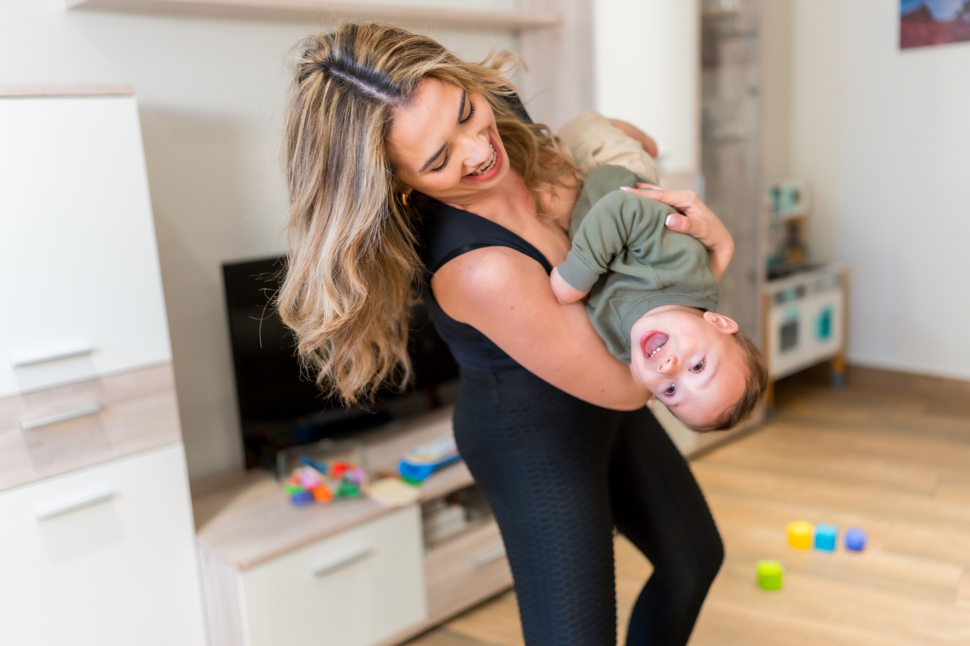 Mother holding her laughing baby upside down at home