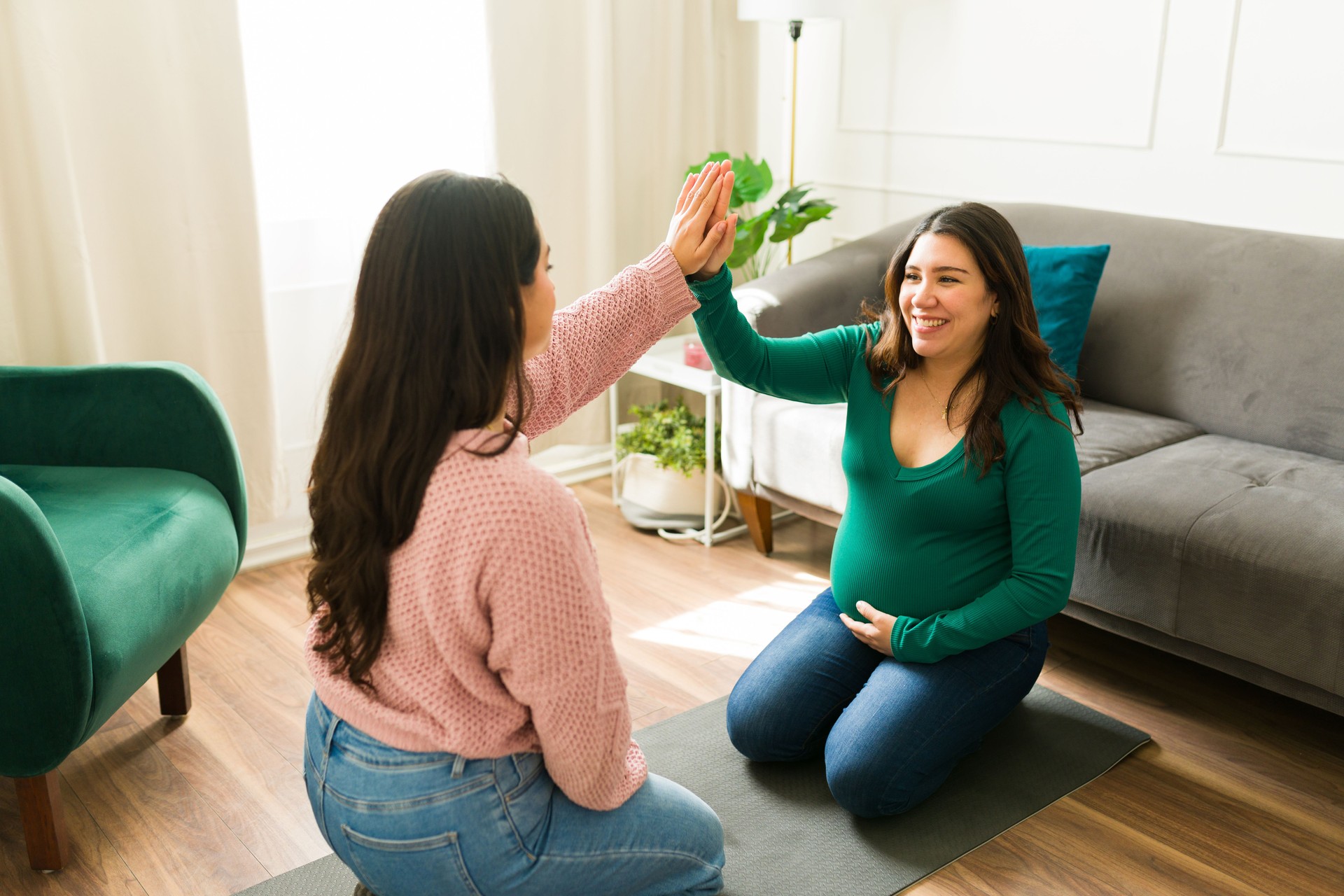 Happy midwife and pregnant woman sharing a joyful high five during a supportive home visit, celebrating connection and trust in motherhood